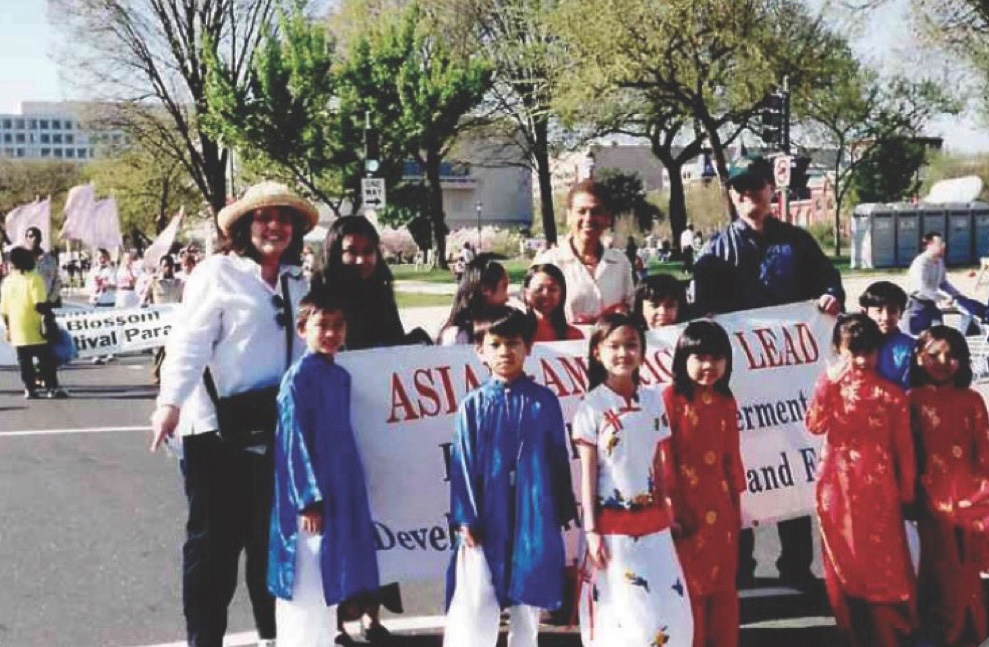 Youth wearing traditional Vietnamese attire hold a Cherry Blossom Festival banner that reads "Asian American LEAD."
