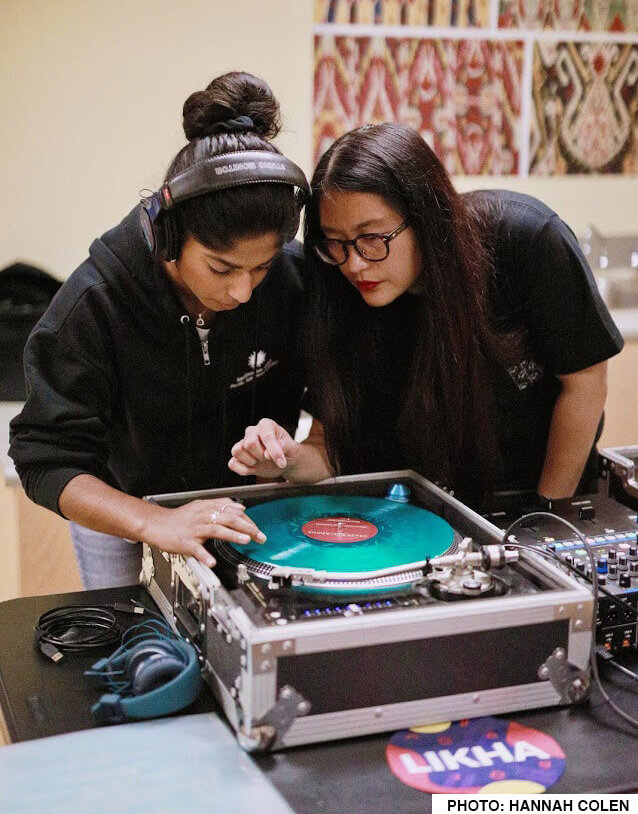 An intern learning from Les the DJ during a youth workshop about deejaying equipment and the creative process